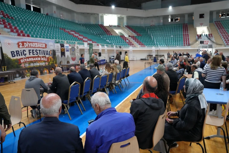 Seyrantepe Spor Salonu'ndaki 2. Diyarbakır Briç Festivali'nde masalarda oturan katılımcılar ve arkada festival afişi