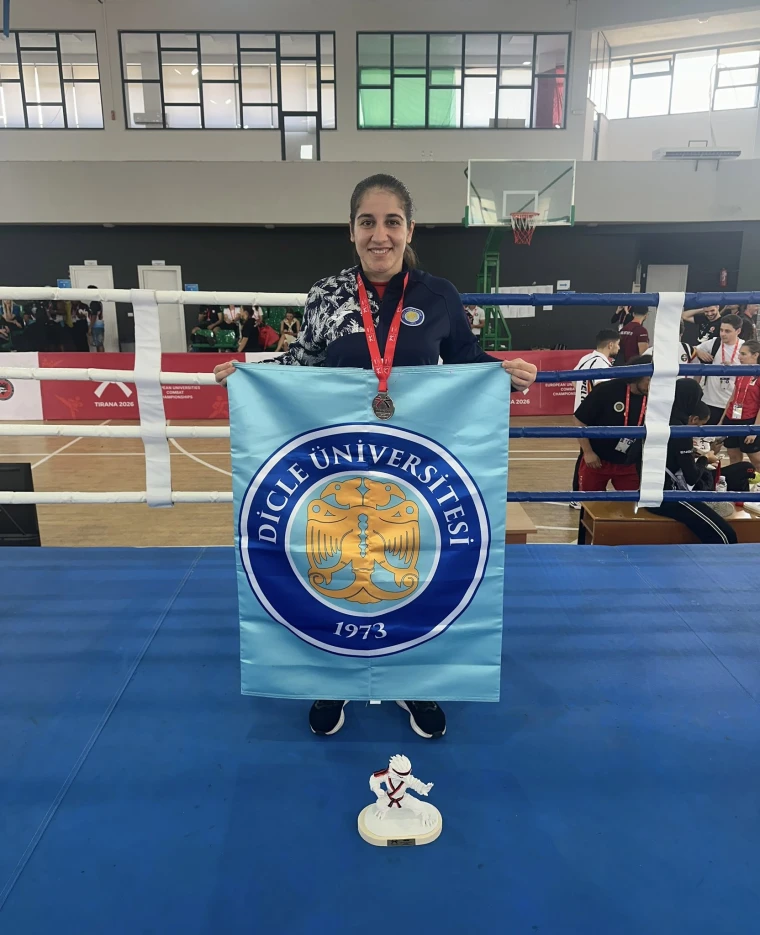 Dilek Erol, boks ringinde Dicle Üniversitesi bayrağını açmış, boynunda madalyasıyla poz veriyor